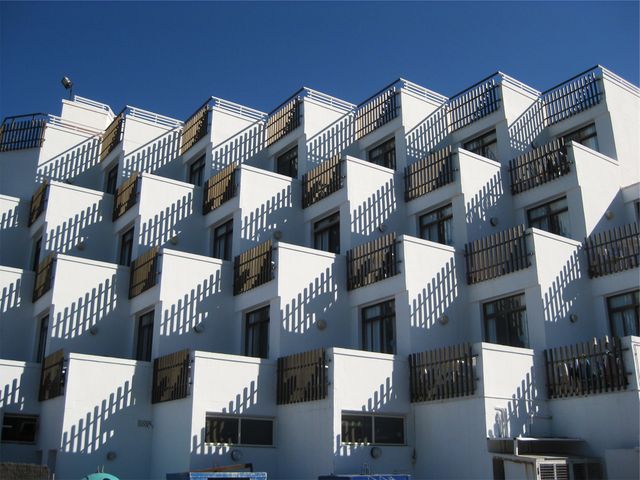 Contemporary white building with balconies casting detailed shadows, perfect for themes about modern architecture, urban living, and design. Ideal for use in articles, design layouts, and real estate promotions.