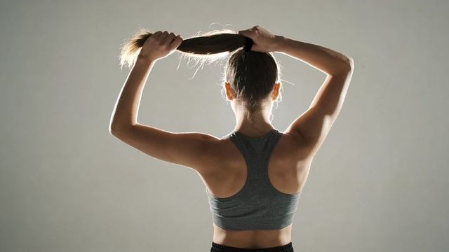 Young woman gathering ponytail backlit fitness portrait showing toned back and sportswear
