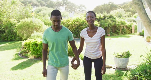 Young couple walking hand-in-hand through a lush garden. They are smiling and looking content, enjoying each other’s company. This is perfect for themes related to romance, dating, relationships, nature, and summer. Can be used for lifestyle, health, and happiness topics in articles, blogs, and advertisements.