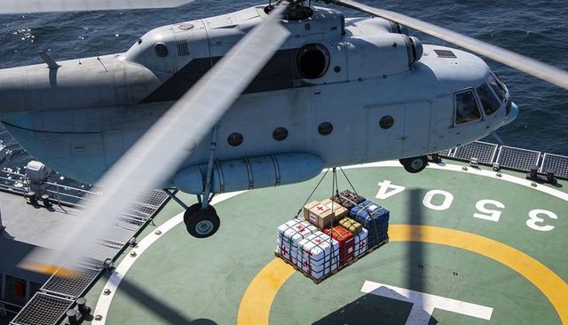 Naval helicopter hovering over helipad lifting medical and supply cargo pallet at sea