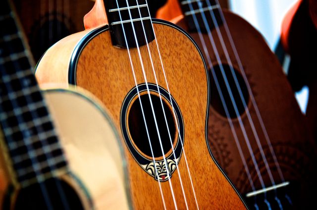Features close-up view of several wooden ukuleles, showcasing intricate craftsmanship and Hawaiian design. Ideal for use in articles about music, cultural traditions, musical instrument sales, and the popularity of ukuleles in modern music.