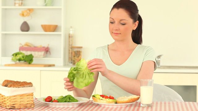 Young woman preparing healthy sandwich with fresh vegetables in a bright kitchen. Perfect for use in articles or marketing materials focusing on healthy eating, cooking at home, health and nutrition, domestic life, and lifestyle blogs.