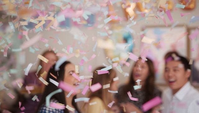 Joyful Friends Celebrating Catching Colorful Confetti Indoors