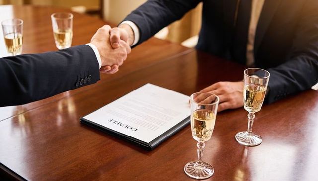Sealing corporate deal with champagne celebration, executives shaking hands at boardroom table