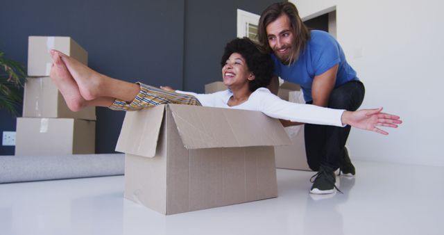 Caucasian man pushing his wife sitting in cardboard boxes at new apartment house. relocation and real estate concept