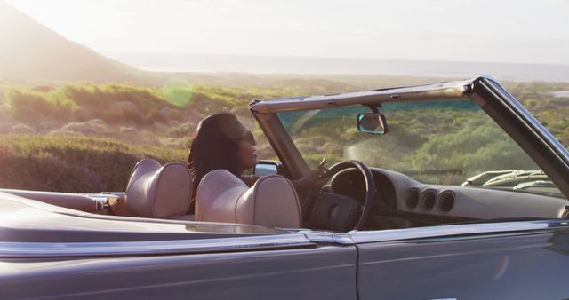 African american woman driving along country road in convertible car. road trip travel and adventure concept