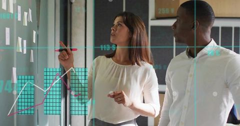 Pointing woman planning on glass wall with red marker while colleague reviewing data charts