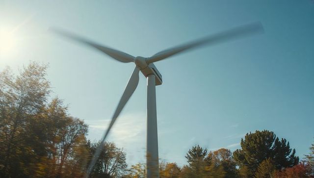 Spinning Wind Turbine in Autumn Forest Under Clear Blue Sky