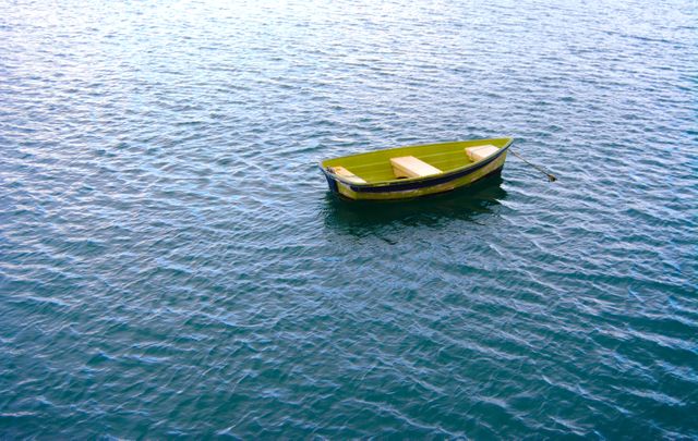 Image shows a small wooden rowboat floating in the middle of calm blue waters. Ideal for themes related to tranquility, peacefulness, relaxation, and nautical adventures. It can be used in travel blogs, nature-related websites, meditation apps, and outdoor adventure promotions.