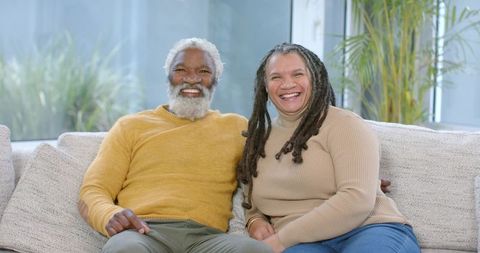 African American Mature Couple Sitting and Smiling on Cozy Sofa in Sunlit Living Room