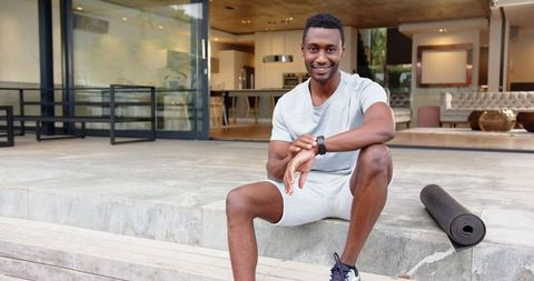 Man relaxing outside home checking smartwatch near yoga mat