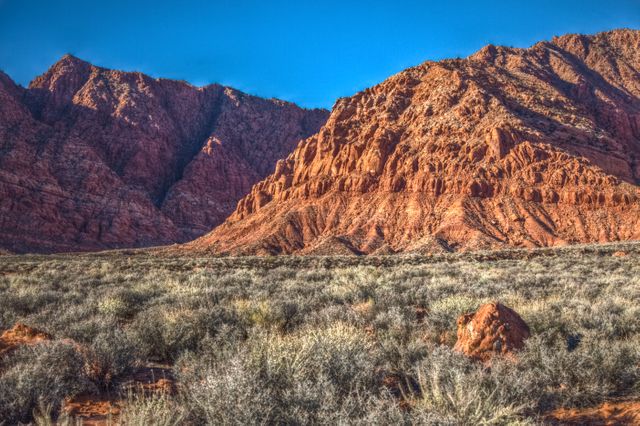Majestic red rock mountain view under a clear blue sky with dry vegetation in the foreground. Ideal for nature tourism promotions, geological studies, outdoor adventure advertisements, and landscape photography collections.