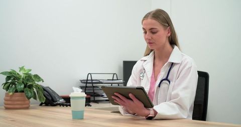 Female doctor reviewing patient records on tablet at modern clinic desk, minimal workspace