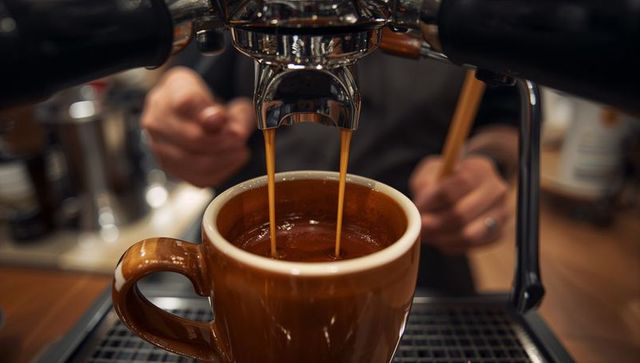 Pulling double espresso into brown ceramic mug showing barista craft at coffee counter