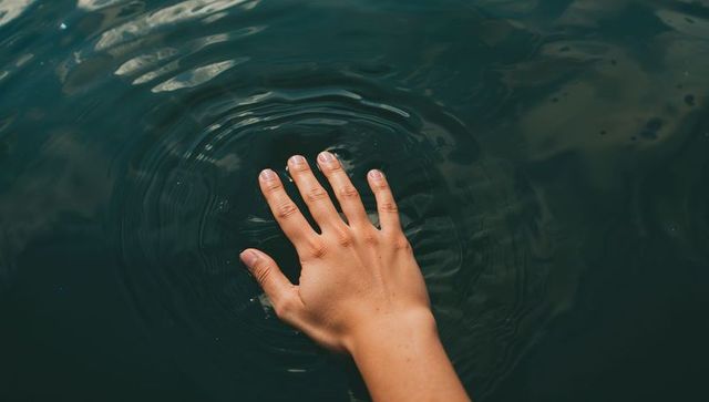 Hand Touching Dark Green Lake Surface Creating Gentle Concentric Ripples Minimalist Calm