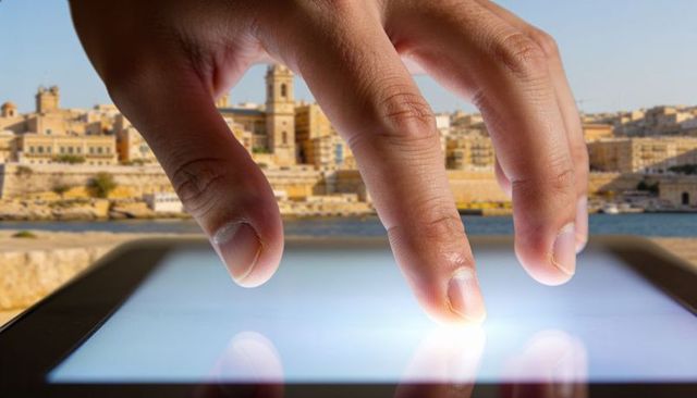 Close-up fingers swiping glowing tablet over coastal harbor with bell tower reflection