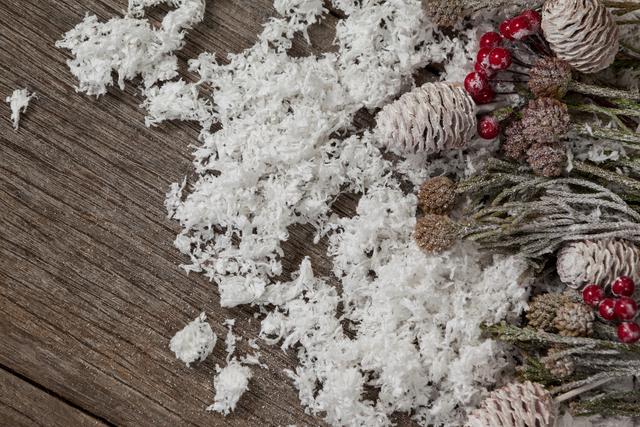 Pine cones and red berries are dusted with fake snow on a rustic wooden plank, creating a festive and natural holiday scene. This image is perfect for use in holiday cards, seasonal advertisements, winter-themed decorations, and as a background for festive designs.
