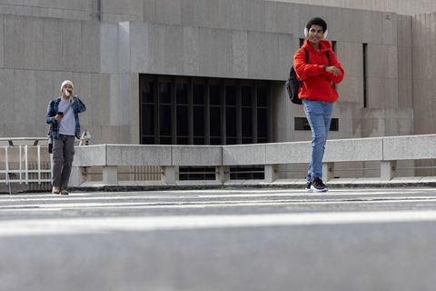 Young men crossing concrete plaza in red hoodie and headphones urban commute scene