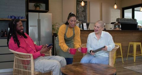 Diverse friends laughing while barista serves red mugs in cozy modern cafe lounge