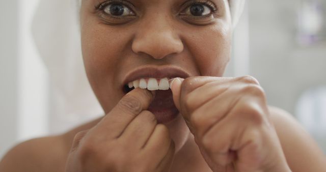 Happy african american woman flossing teeth and using smartphone in bathroom. domestic lifestyle, spending free time at home.