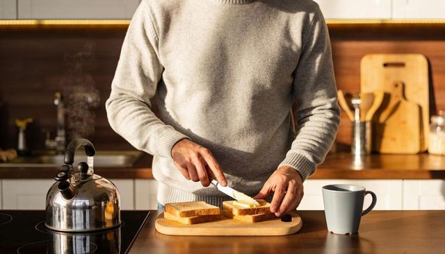 Man spreading butter on toast at kitchen counter in cozy morning light