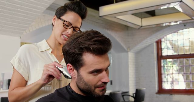 A young Caucasian female hairstylist is giving a haircut to a young Caucasian male client in a modern barbershop, with copy space. Her professional expertise is evident as she carefully styles his hair, ensuring a tailored and fashionable look.