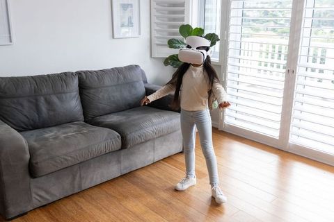 Young girl wearing vr headset exploring virtual reality in bright modern living room