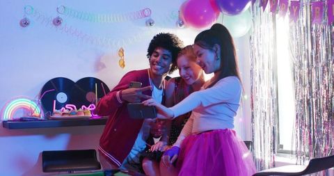 Diverse friends taking selfie at colorful birthday party with balloons and neon decor