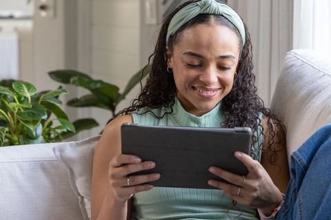 African american woman relaxing on couch using tablet in sunlit living room