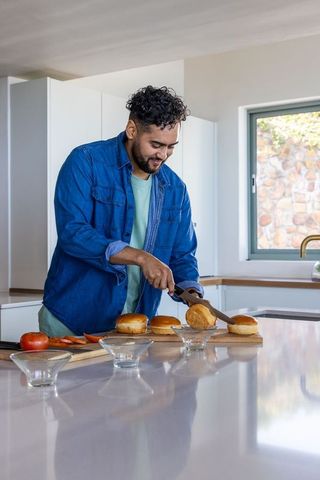 Man slicing burger buns on kitchen island preparing homemade burgers in modern kitchen