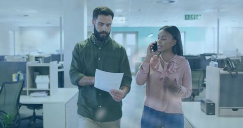 Two Coworkers Walking Through Open Office Consulting Document While Talking on Phone