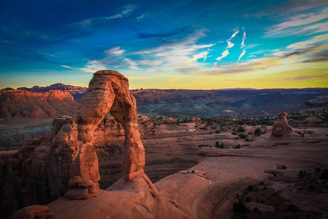 Sunset over iconic Delicate Arch in Arches National Park, Utah captures dramatic sandstone formations against a colorful sky. Ideal for use in travel brochures, nature magazines, and educational geography materials highlighting natural wonders of the American Southwest.