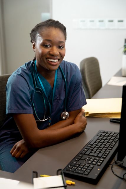 Portrait of smiling african american female doctor sitting at desk with computer. Medical services, hospital and healthcare concept.