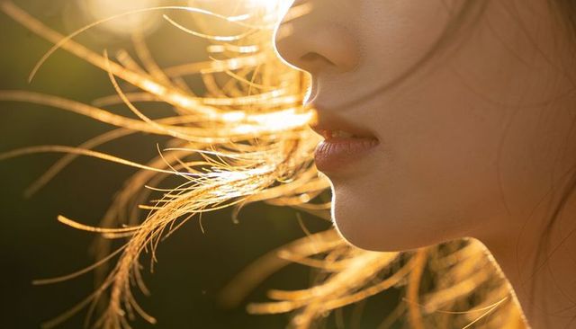 Backlit close-up of woman's lips and jawline with golden hour hair rimlight