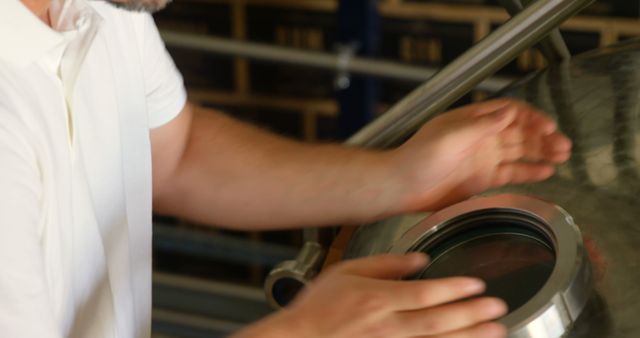 Worker in a brewery checking the lid of a fermentation vat, crucial for craft beer production. Useful for illustrating processes in beer manufacturing, brewing industry operations, or quality control in food and beverage production.