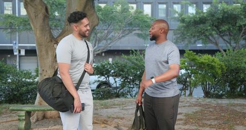Two friends chatting after workout holding duffel bags in urban park fitness lifestyle