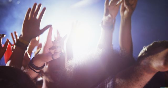 A diverse group of people are enjoying a concert, raising their hands in the air with bright stage lights in the background. The image captures the energetic atmosphere of a live music event, with fans celebrating and enjoying the performance.