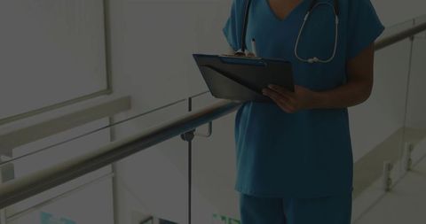 Nurse checking clipboard on hospital mezzanine with stethoscope and daylight
