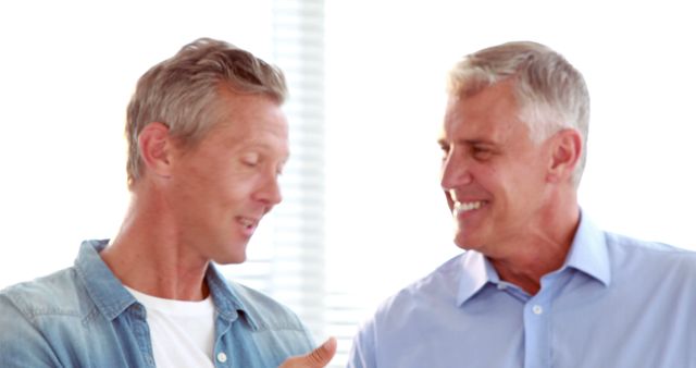 Two middle-aged Caucasian men are engaged in a friendly conversation, with copy space. Their relaxed body language and smiles suggest a positive interaction or agreement.