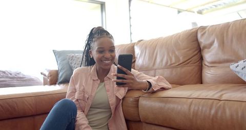 Young Woman Smiling at Phone Sitting in Modern Living Room