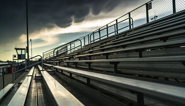 Empty aluminum bleachers stretching under dramatic storm clouds at outdoor stadium