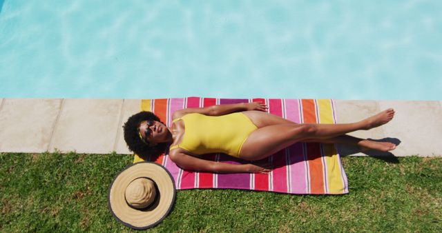 Biracial woman lying on blanket sunbathing by the pool. hanging out and relaxing outdoors in summer.