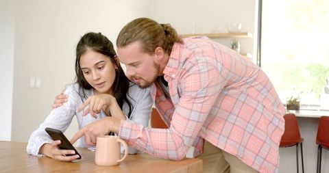 Young Couple Engaging with Smartphone in Bright Kitchen
