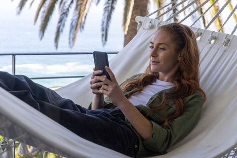 Woman Relaxing in Hammock with Smartphone by Ocean
