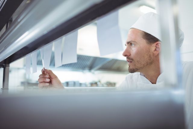 Chef reviewing an order list in a commercial kitchen, ideal for illustrating restaurant operations, culinary professions, and kitchen management. Useful for articles, blogs, and advertisements related to the food industry, professional cooking, and restaurant business.