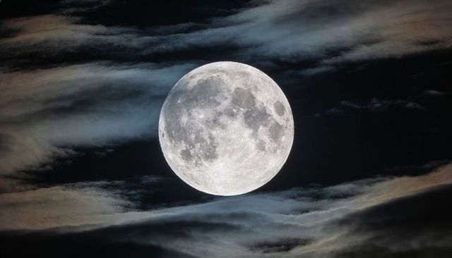 Glowing full moon revealing lunar craters drifting through layered clouds