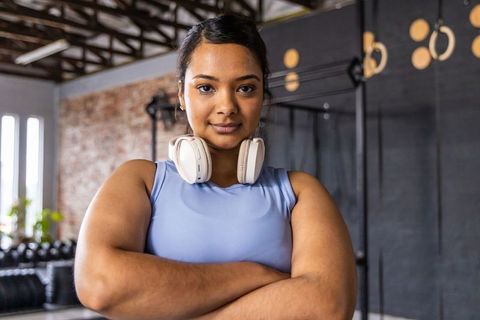 Indian woman standing confidently with arms crossed in industrial gym wearing headphones