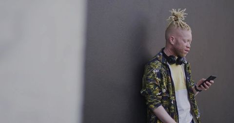 Fashionable male with albino skin checking smartphone outdoors