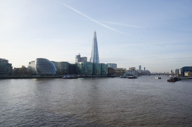 Depicts scenic London waterfront view featuring Thames River with Shard and surrounding modern buildings on a clear day. Ideal for travel brochures, London tourism promotions, website backgrounds highlighting London skyline, urban development articles, and editorial pieces on iconic architecture with a focus on the Shard and other prominent buildings along the Thames.
