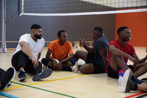 African american men sitting and chatting on indoor volleyball court showing team camaraderie